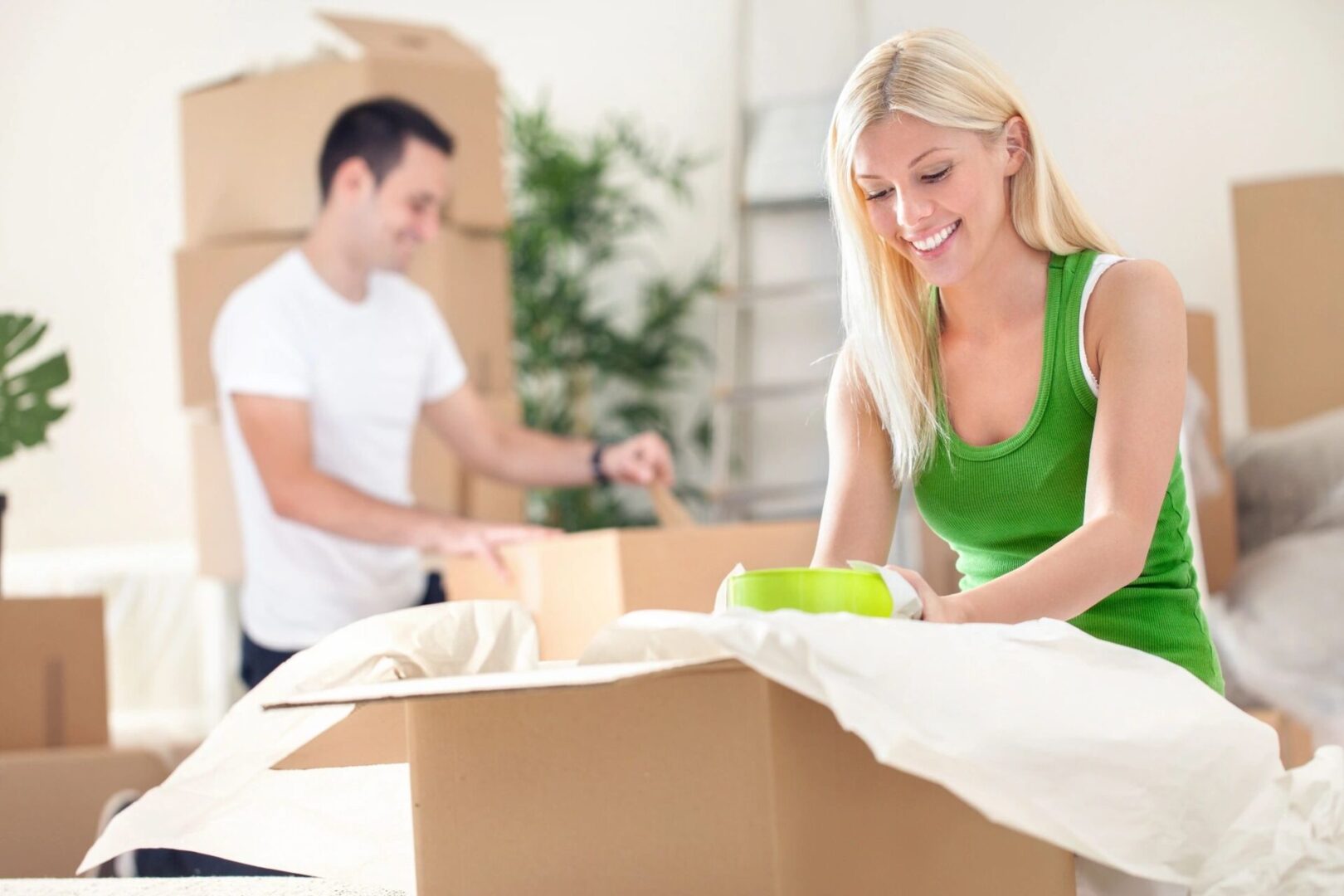 A woman in green shirt and man in white shirt packing boxes.